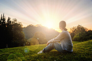 Girl sits on meadow watching the sunset in the mountains