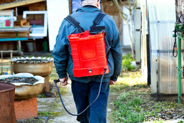 Modern red sprayer on the back of a male summer resident for treating bushes in spring, close-up....