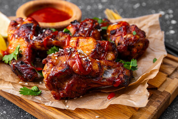 Grilled spicy chicken wings with ketchup on a dark grey background close up