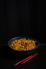 Top view of a bowl of noodles and chopsticks on a table with a black background, vertically with copy space