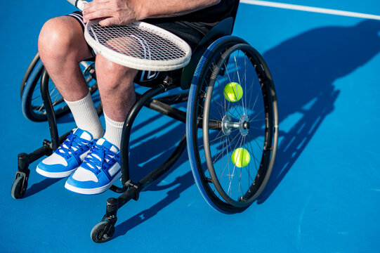 A wheelchair tennis player sits ready for action, his racquet poised and tennis balls nearby