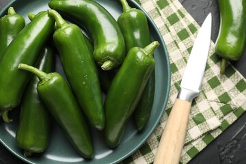 Fresh jalapeno peppers and knife on black table, above view