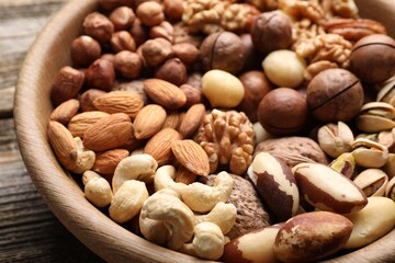 Mix of different nuts in bowl on wooden table, closeup