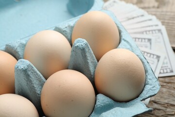 Raw chicken eggs in egg carton and dollar banknotes on table, closeup