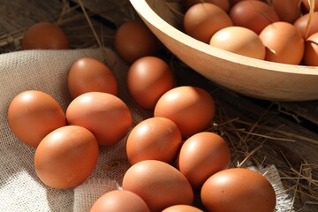 Raw chicken eggs and straw on wooden table, closeup