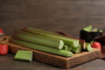 Fresh rhubarb stalks and strawberries on wooden table, closeup