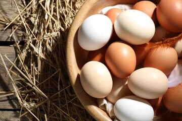 Raw chicken eggs, feathers and straw on wooden table, top view