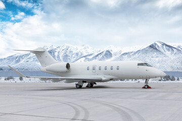 Naklejka premium White corporate airplane at winter airport on background of high scenic snow capped mountains