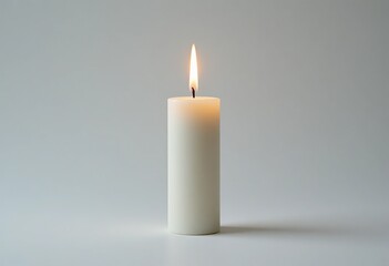 Lit white pillar candle with a bright warm flame on a clean light grey background, isolated studio shot