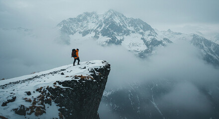 Adventurer on the edge of a snowy cliff, looking at cloudy mountain peaks,
