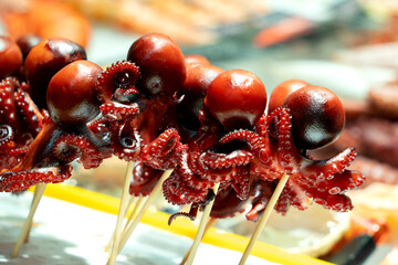 Skewered baby octopus street food, vibrant red seafood delicacy on sticks, popular in Japanese night markets and Asian culinary culture © Denise