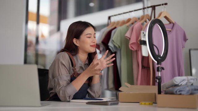 Asian adult woman entrepreneur live stream sell clothes online home studio digital marketing promote business fashion apparel social media success retail commerce
