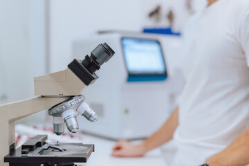 A scientist in a white shirt analyzes samples through a microscope in a modern laboratory setting.