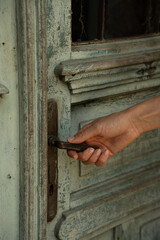 Hand opening old wooden door. Close-up of human hand opening vintage wooden door with weathered paint. Concept of entering, exploring, tourism, safety and lifestyle.