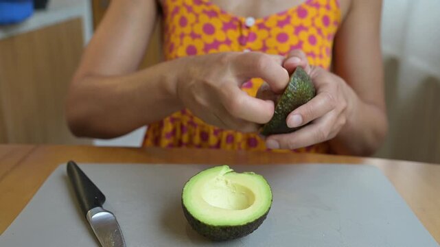 Close-up video of a person cutting a fresh avocado in half, showing the seed and pulp on a kitchen cutting board during meal preparation