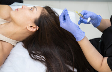 Caucasian female mature patient getting head or scalp injection in cosmetology clinic. Receding hairline, baldness problems, hairloss. Cosmetologist doing injections with syringe. 