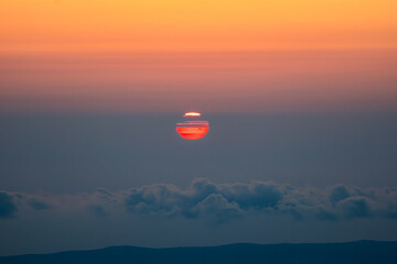 Extreme Close-up of the Sun Setting Over Clouds and Mountains with Fiery Sky Colors