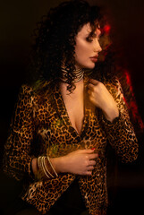 Beautiful young woman in clothes with animal prints and beige boots sits in the studio. Portrait of a girl with curls, 90s style. Mixed color neon light, double exposure, selective focus.
