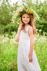 Cute smiling little girl  with flower wreath on the meadow at the farm. Portrait of adorable small kid outdoor.