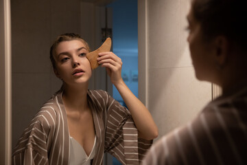 Beautiful young woman taking care of her face at home, skincare procedures, selective focus. Portrait of a woman applying a serum and doing face massage for her face in her bathroom. Real photo.