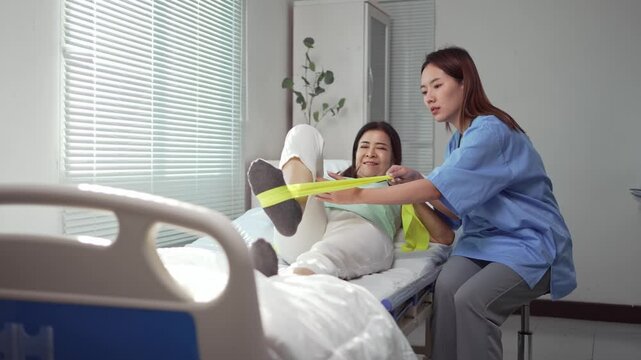 Experienced physiotherapist assisting elderly woman with resistance band physical therapy in hospital room