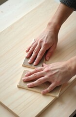 Hands sand wooden surface using sandpaper. Two sanding blocks smoothing timber. Person works in carpentry shop. Woodworker grinds plank. Master at work. Sanding to improve surface, remove unevenness.