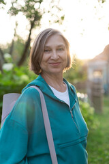 Happy smiling active mature woman in blue sportswear with yoga mat on her shoulder outdoors. Sport training concept