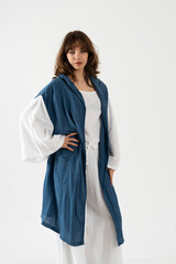 Stylish young woman posing confidently in white wide sleeve outfit and long hooded blue vest.