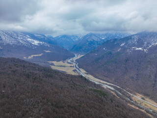 Obraz premium Drone view over a vast, deep valley covered in bare, dark trees, with a river and road winding through the valley floor beneath cloudy skies