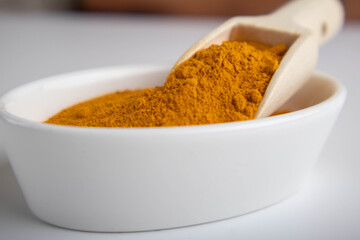 ground turmeric in a wooden spoon on white background