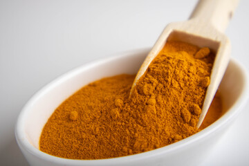 ground turmeric in a wooden spoon on white background