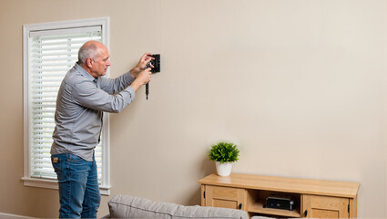 Elderly man screwing in TV mount on wall in living room  