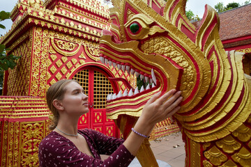A Young Woman Interacting with a Brightly Colored DragonSculpture in Front of a Decorative Temple in an Enchanting Cultural Setting