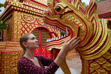 A Young Woman Interacts with a Beautifully Crafted Golden Dragon Sculpture in a Vibrant Temple Setting, Showcasing Cultural Artistry and Architectural Grandeur.