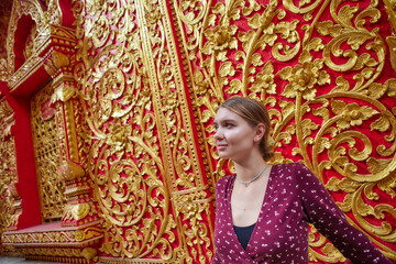 A Young Woman Poses Elegantly Against a Vibrant Red and Gold Ornate Wall Featuring Intricate Floral Patterns and Decorative Elements