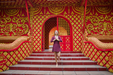Fototapeta premium A Graceful Woman in a Purple Dress Offering a Gesture of Respect Amidst Vibrant Red and Gold Architectural Features