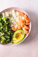 A nutritious breakfast bowl featuring rice, salmon, avocado, and fresh greens is presented beautifully in a bowl. Simple and healthy morning meal idea with vibrant colors