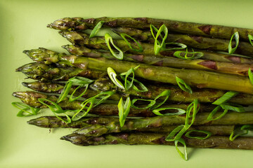 Asparagus spears are arranged neatly on a green plate, garnished with sliced green onions. This dish represents a simple yet flavorful vegetable choice for any meal
