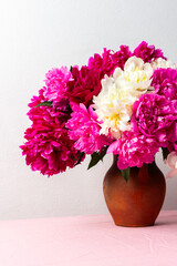 A vibrant arrangement of pink and white peonies fills a ceramic vase, placed on a soft pink tablecloth. The flowers add a cheerful touch to any room, ideal for spring decor