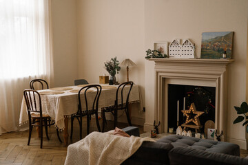 Cozy dining room with Christmas decor. Minimalist dining room with a linen-covered table, vintage chairs and a decorated fireplace with a glowing star light. Warm cozy holiday atmosphere