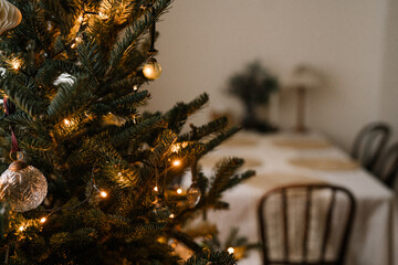 Minimalist Christmas tree with golden ornaments and warm fairy lights in a cozy dining room setting.