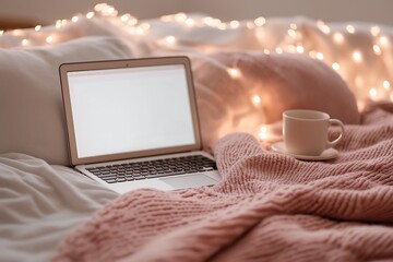 A warm bedroom setting with a laptop on a bed, a cup of coffee, a soft knitted blanket, and glowing fairy lights