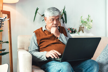 Senior Man Sitting on Sofa Using Laptop in Modern Home Environment Illustrating Digital Connection, Retirement Lifestyle, Online Communication, and Concentrated Learning