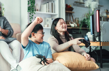 Asian Siblings Playing Console Video Game Together in Cozy Living Room Showing Family Bond, Technology, Fun Childhood, and Joyful Modern Lifestyle