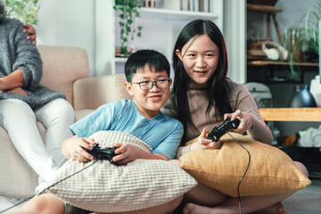 Asian Siblings Playing Console Video Game Together in Cozy Living Room Showing Family Bond, Technology, Fun Childhood, and Joyful Modern Lifestyle