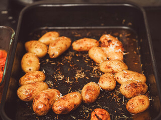 Cooked full uncut potatoes on a dark metal tray with herbs. Fine dinner side dish ready to be served. Home cooking concept.