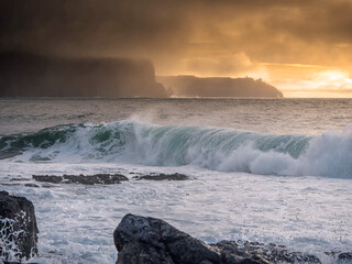 Dramatic nature scene with ocean waves, rough stone coast, cliffs and dark sunset sky. Doolin area, Ireland. Famous tourist area. Irish landscape.