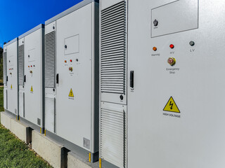 A row of outdoor high-voltage electrical cabinets with warning labels, ventilation panels, and...