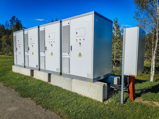 A row of outdoor high-voltage electrical cabinets with warning labels, ventilation panels, and emergency stop buttons under a clear blue sky.