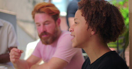 Diverse Family members enjoying a lively meal outdoors, featuring an African American senior laughing and interacting while a Hispanic Latin teenager joins the conversation